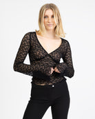 Model trägt eine schwarzes Langarmshirt aus zarter Spitze mit V-Ausschnitt und Brustabnähern.