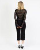 Model trägt eine schwarzes Langarmshirt aus zarter Spitze mit V-Ausschnitt und Brustabnähern zu einer schwarzen Caprihose und schwarzen Schnür Ballerinas und weißen Socken.