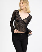 Model trägt eine schwarzes Langarmshirt aus zarter Spitze mit V-Ausschnitt und Brustabnähern zu einer schwarzen Caprihose.