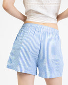 Model trägt eine luftige Shorts mit blauen Streifen und mit Bindebändern, elastischem Bund und weitem Schnitt.