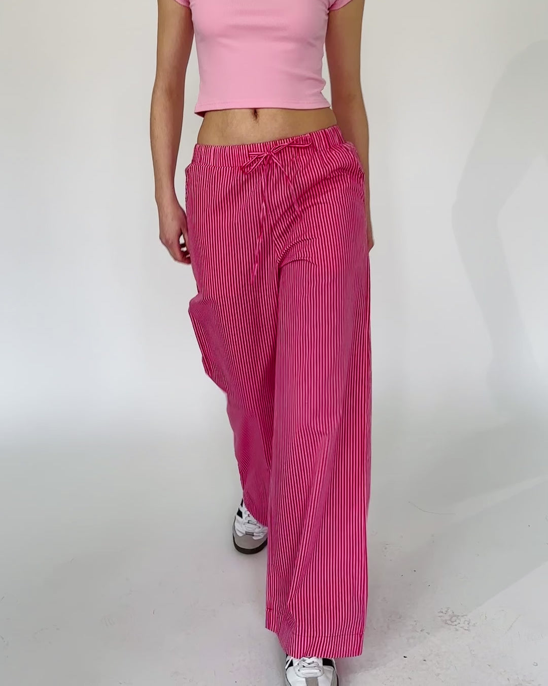 Model trägt eine pink gestreifte Baumwollhose zu einem rosa bauchfreien T-Shirt.