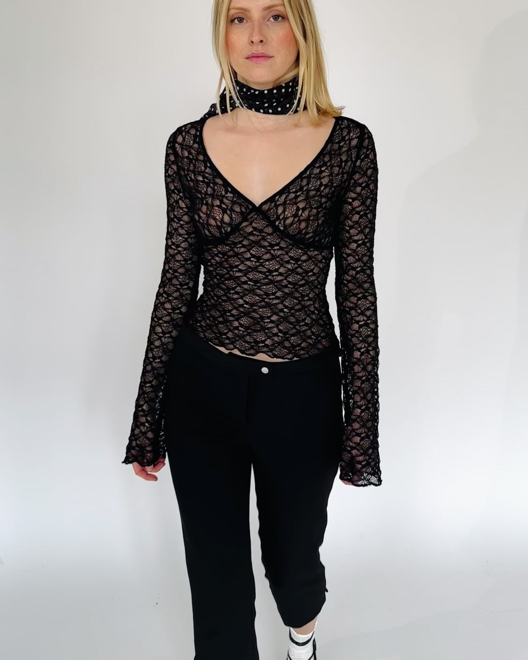 Model trägt eine schwarzes Langarmshirt aus zarter Spitze mit V-Ausschnitt und Brustabnähern zu einer schwarzen Caprihose.