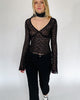 Model trägt eine schwarzes Langarmshirt aus zarter Spitze mit V-Ausschnitt und Brustabnähern zu einer schwarzen Caprihose.