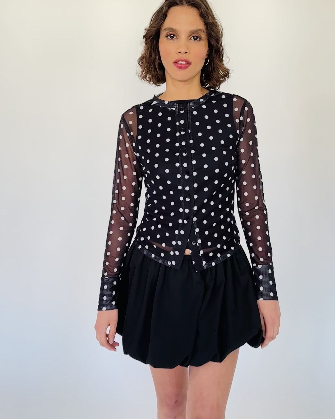 Model trägt einen schwarzen Mesh Cardigan mit Polkadotprint zu einem schwarzen Ballon Rock.