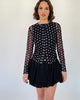 Model trägt einen schwarzen Mesh Cardigan mit Polkadotprint zu einem schwarzen Ballon Rock.